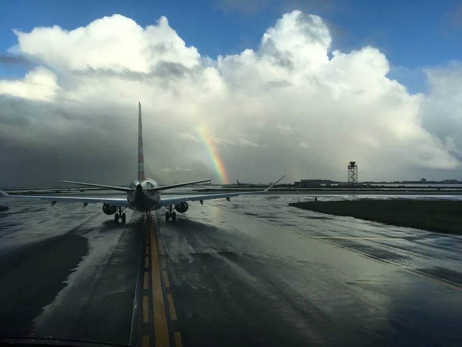 View from the cockpit of an airliner taxiing on a rain-soaked runway beneath a rainbow